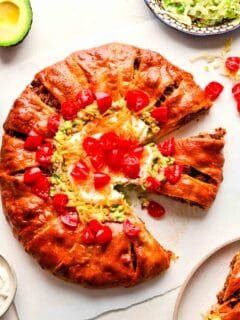 baked taco ring with guacamole, diced tomatoes, sour cream, and cheddar cheese in the center