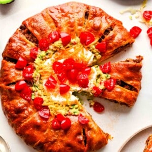 baked taco ring with guacamole, diced tomatoes, sour cream, and cheddar cheese in the center