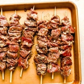 beef pieces skewered on wooden skewers and placed on a metal baking sheet