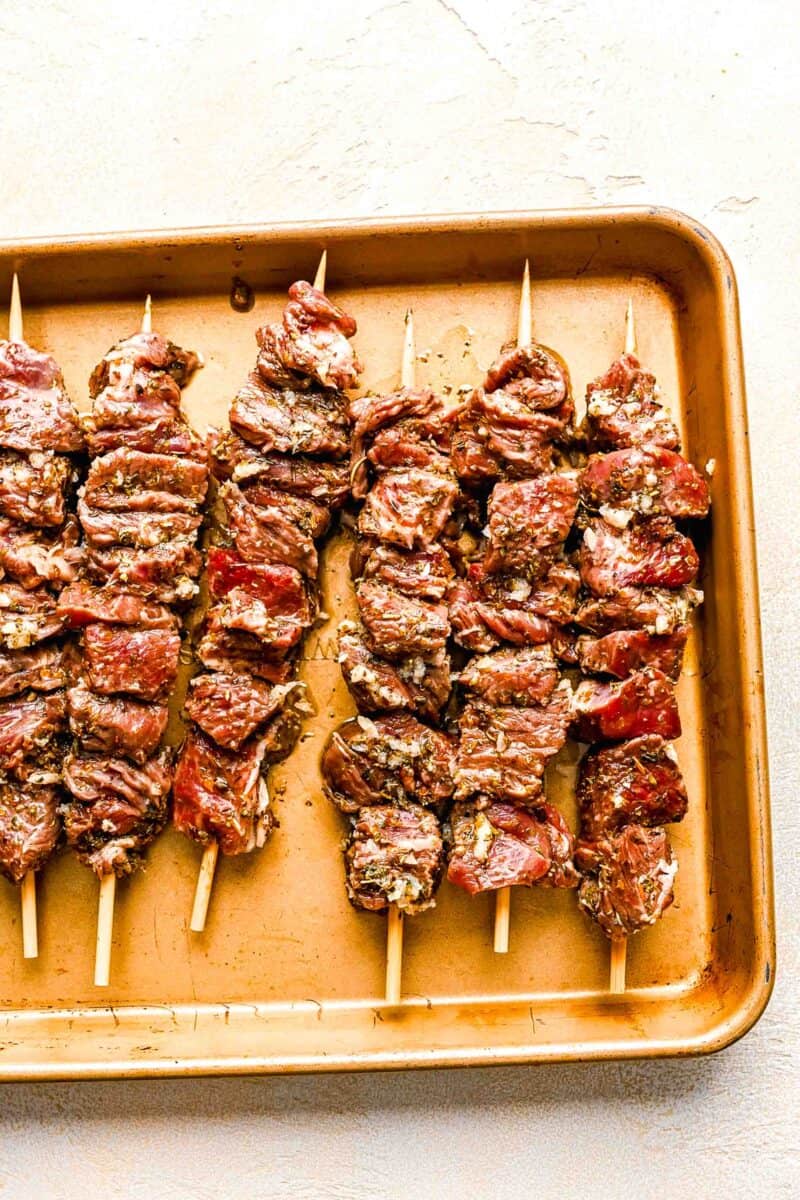 beef pieces skewered on wooden skewers and placed on a metal baking sheet
