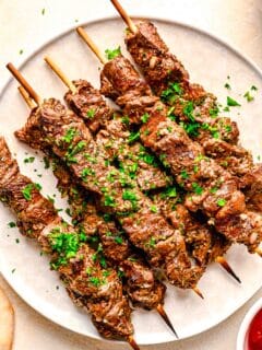 skewered beef souvlaki on a white plate with fresh parsley sprinkled on top as garnish