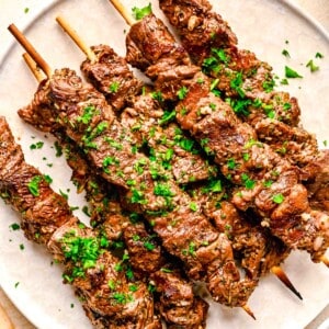 skewered beef souvlaki on a white plate with fresh parsley sprinkled on top as garnish