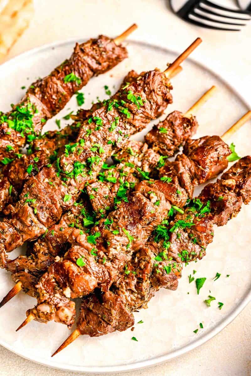 beef souvlaki on wooden skewers on a white plate with fresh parsley sprinkled on top