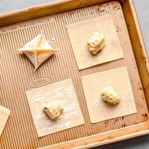 cream cheese mixture in the center of square wonton wrappers on a metal baking sheet