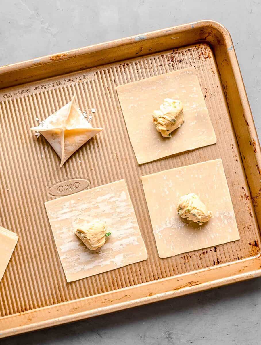 cream cheese mixture in the center of square wonton wrappers on a metal baking sheet