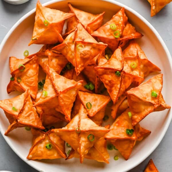 deep fried cream cheese wontons on a large white plate with fresh scallions on top