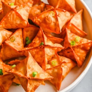 cream cheese wontons on a white plate with green scallions on top