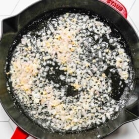 onion and garlic being cooked in a red cast iron skillet