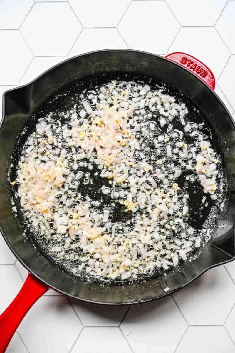 onion and garlic being cooked in a red cast iron skillet