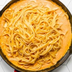 cooked fettuccine pasta placed on top of pumpkin alfredo mixture in the red cast iron skillet