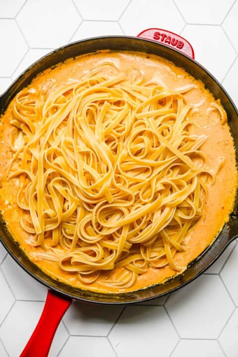 cooked fettuccine pasta placed on top of pumpkin alfredo mixture in the red cast iron skillet