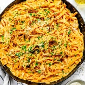 pumpkin alfredo pasta topped with fresh parsley in a red cast iron skillet next to a green glass and linen towel