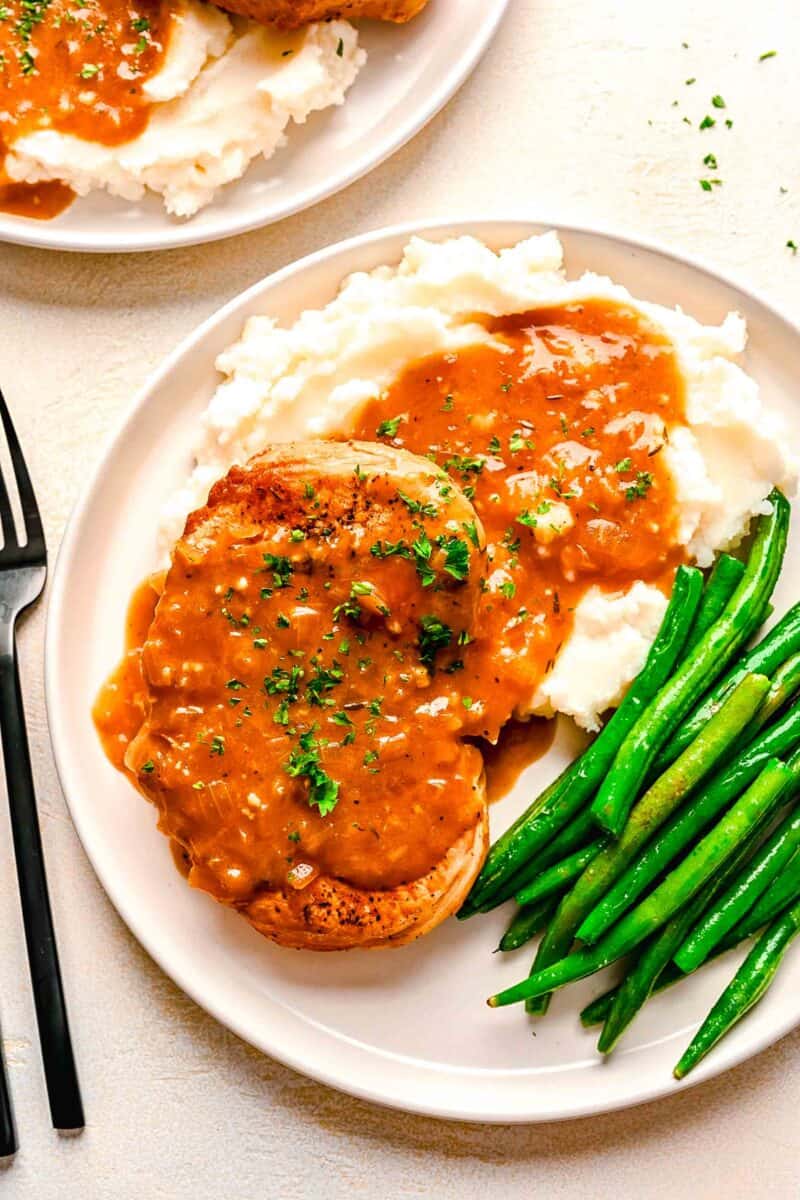 pork chop loin on a bed of mashed potatoes with gravy on top next to freshly cooked green beans