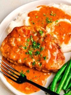 pork chops next to mashed potatoes and green beans with pan drippings made into a gravy on top