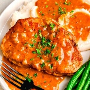 pork chops next to mashed potatoes and green beans with pan drippings made into a gravy on top