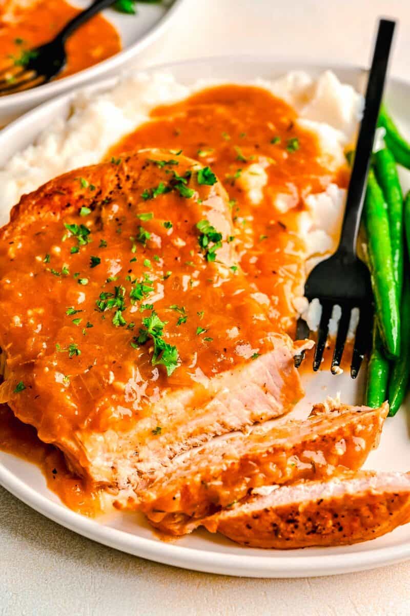 sliced pieces of pork chop with gravy on a plate with a black fork