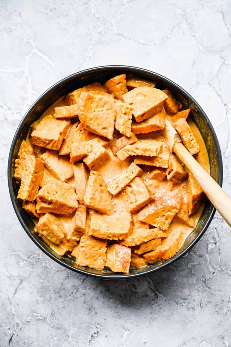 cubed bread pieces in a black bowl with pumpkin egg mixture poured on top