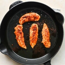 chicken tenderloins being browned and cooked in a cast iron skillet