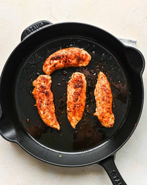 chicken tenderloins being browned and cooked in a cast iron skillet