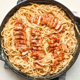 sliced chicken tenderloins on top of pasta in a cast iron skillet