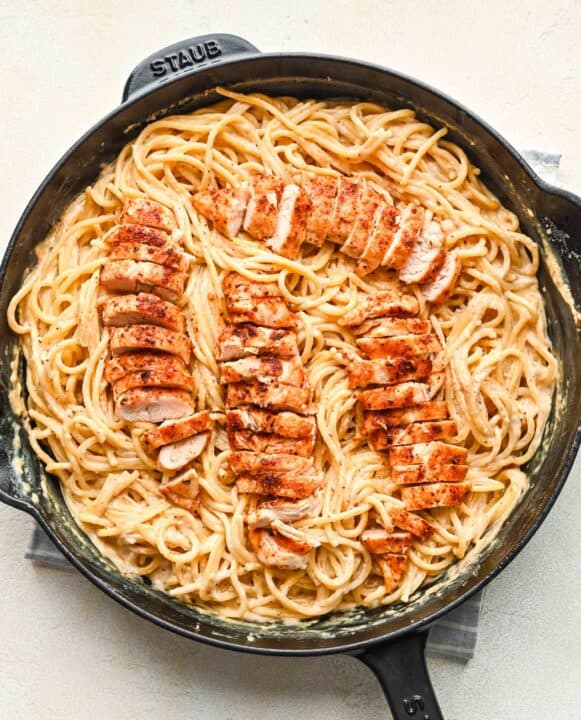 sliced chicken tenderloins on top of pasta in a cast iron skillet