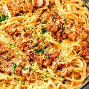 cajun chicken alfredo with sliced chicken on top of pasta in cast iron skillet