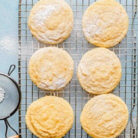 Lemon cookies on a cooling rack dusted with powdered sugar.