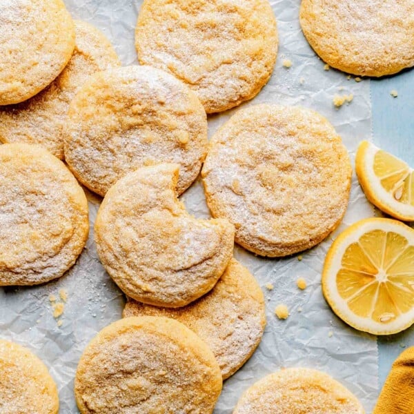 Lemon cookies spread out over parchment paper. One has a bite taken out of it.