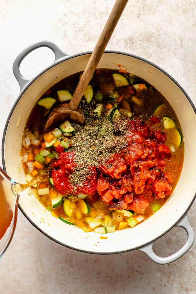 Stirring diced tomatoes, vegetable broth, tomato paste, and Italian seasoning into minestrone soup.