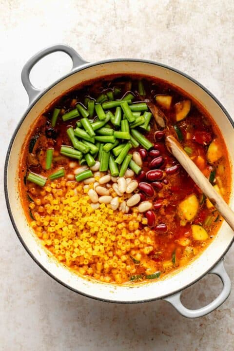 Stirring beans, green beans, and pasta into minestrone soup.