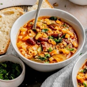 A bowl of minestrone soup with a spoon in it.