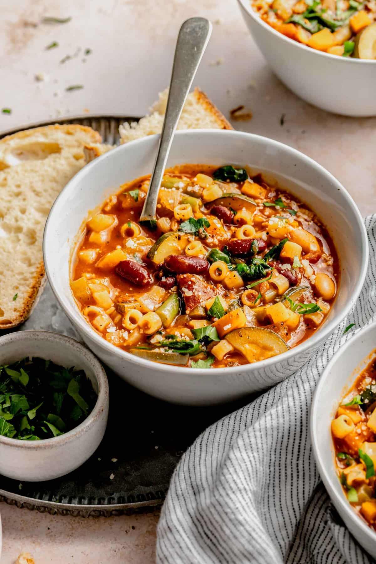 A bowl of minestrone soup with a spoon in it.