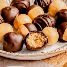 Peanut butter balls on a plate. One has a bite taken out of it.