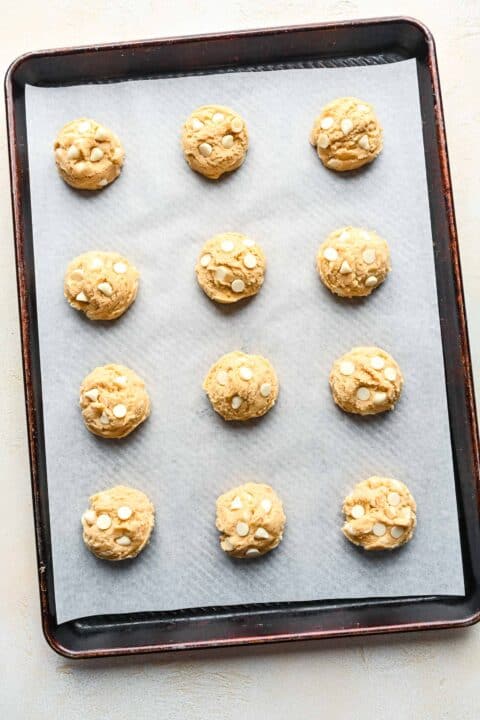 white chocolate chip cookie dough on a metal baking sheet with parchment paper