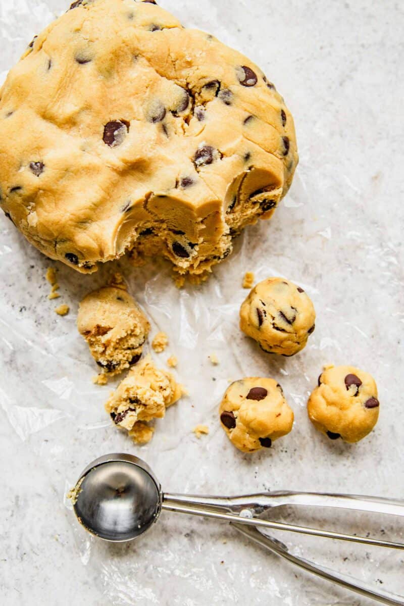Scooping cookie dough balls out of a heap of chocolate chip cookie dough.