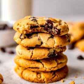 A stack of chocolate chip cookies. The top cookie has a bite taken out of it.