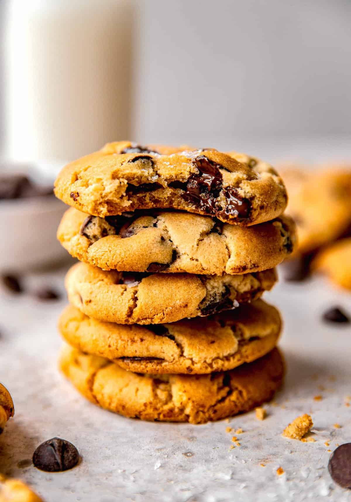A stack of chocolate chip cookies. The top cookie has a bite taken out of it.