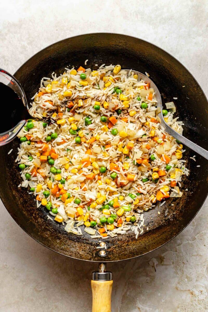 Adding soy sauce to fried rice in a wok.