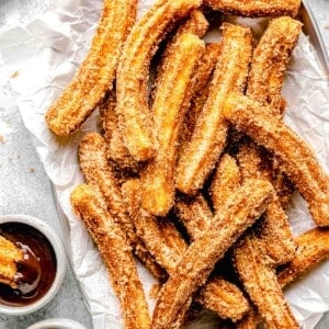 mexican churros on a metal platter next to dipping sauces