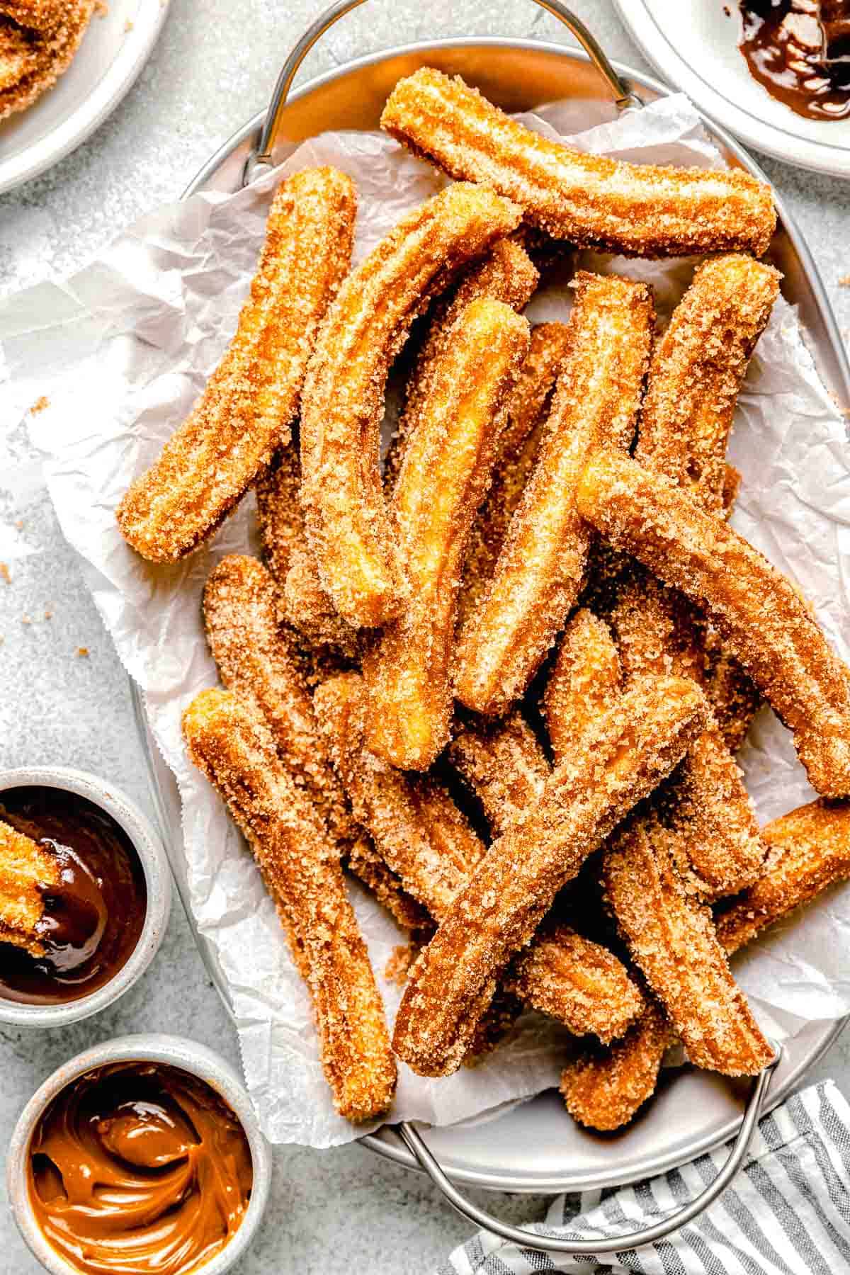 mexican churros on a metal platter next to dipping sauces