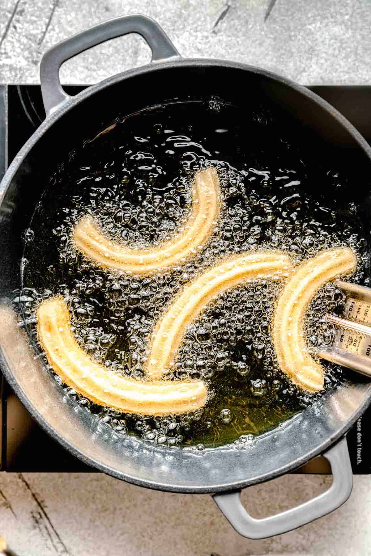 fried churro dough in a cast iron pot with hot oil