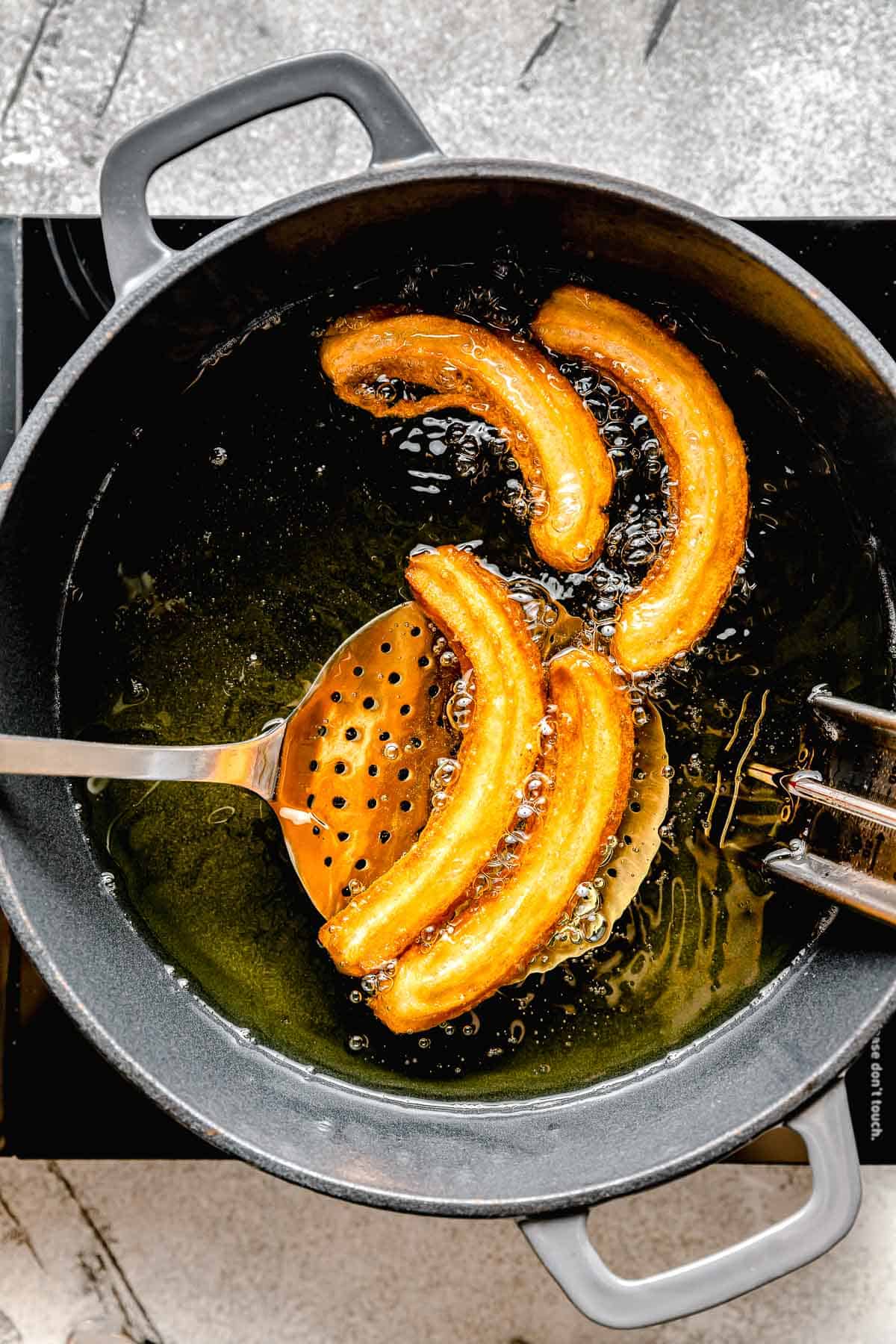 fried churros being scooped out of hot oil with a metal slotted spoon