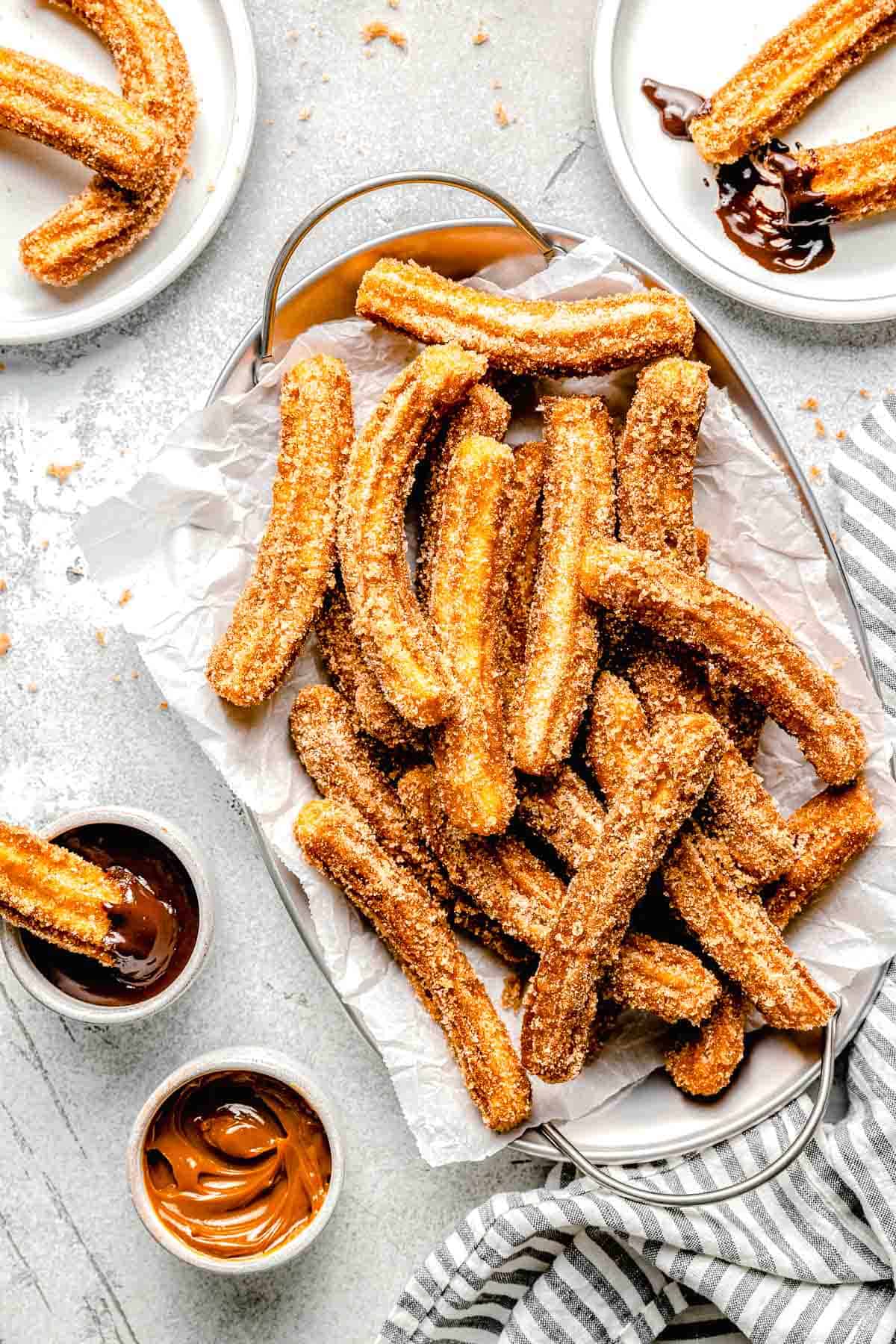 mexican churros on a metal platter with parchment paper next to caramel sauce and chocolate sauce