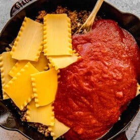 Stirring lasagna noodles and marinara sauce into a skillet with browned sausage, onions, and garlic.