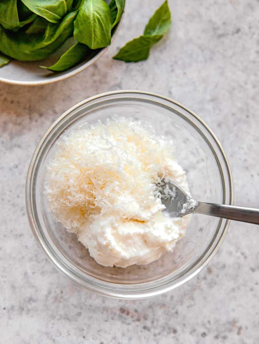 Adding ricotta and grated parmesan to a mixing bowl.