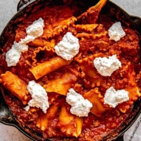 Adding dollops of ricotta and parmesan to skillet lasagna.