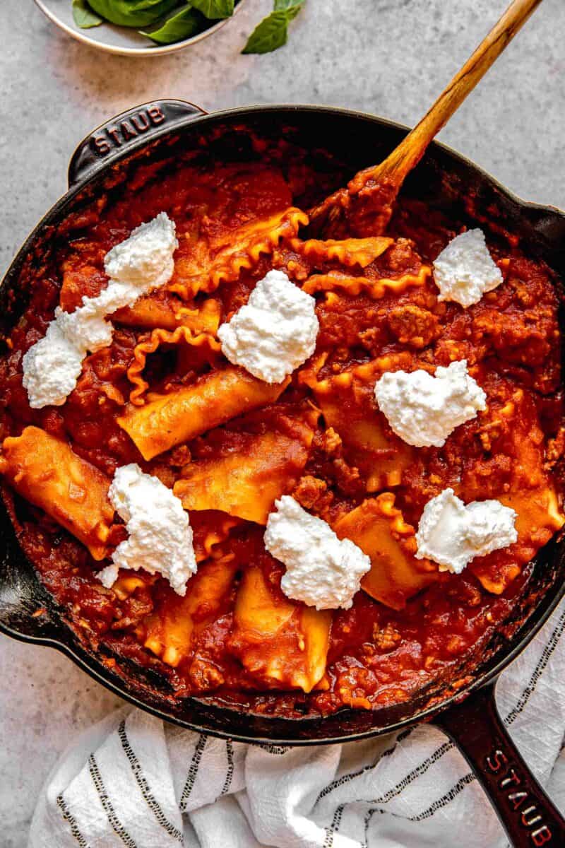 Adding dollops of ricotta and parmesan to skillet lasagna.