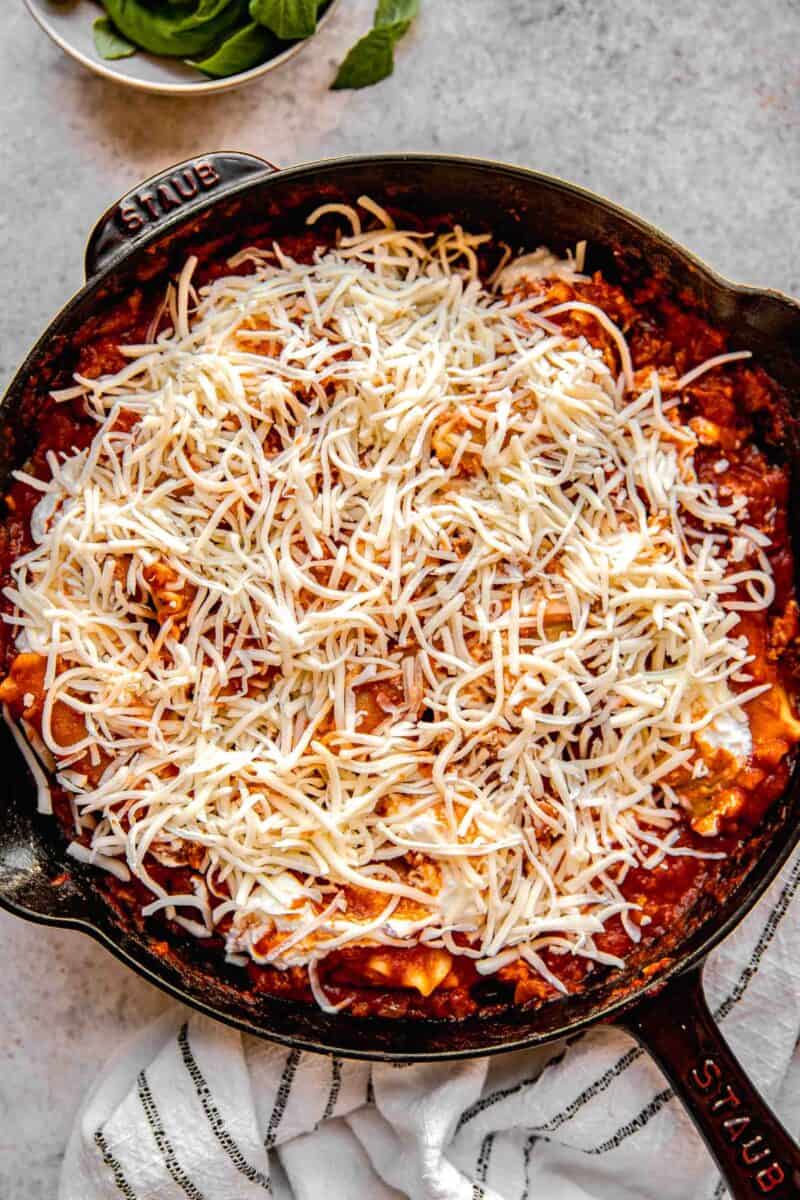 Adding shredded cheese to skillet lasagna.