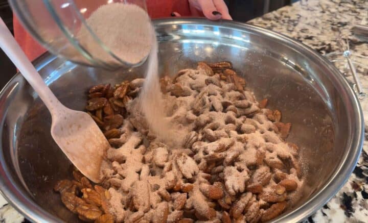 sprinkling cinnamon spice mixture on top of nuts in a metal bowl
