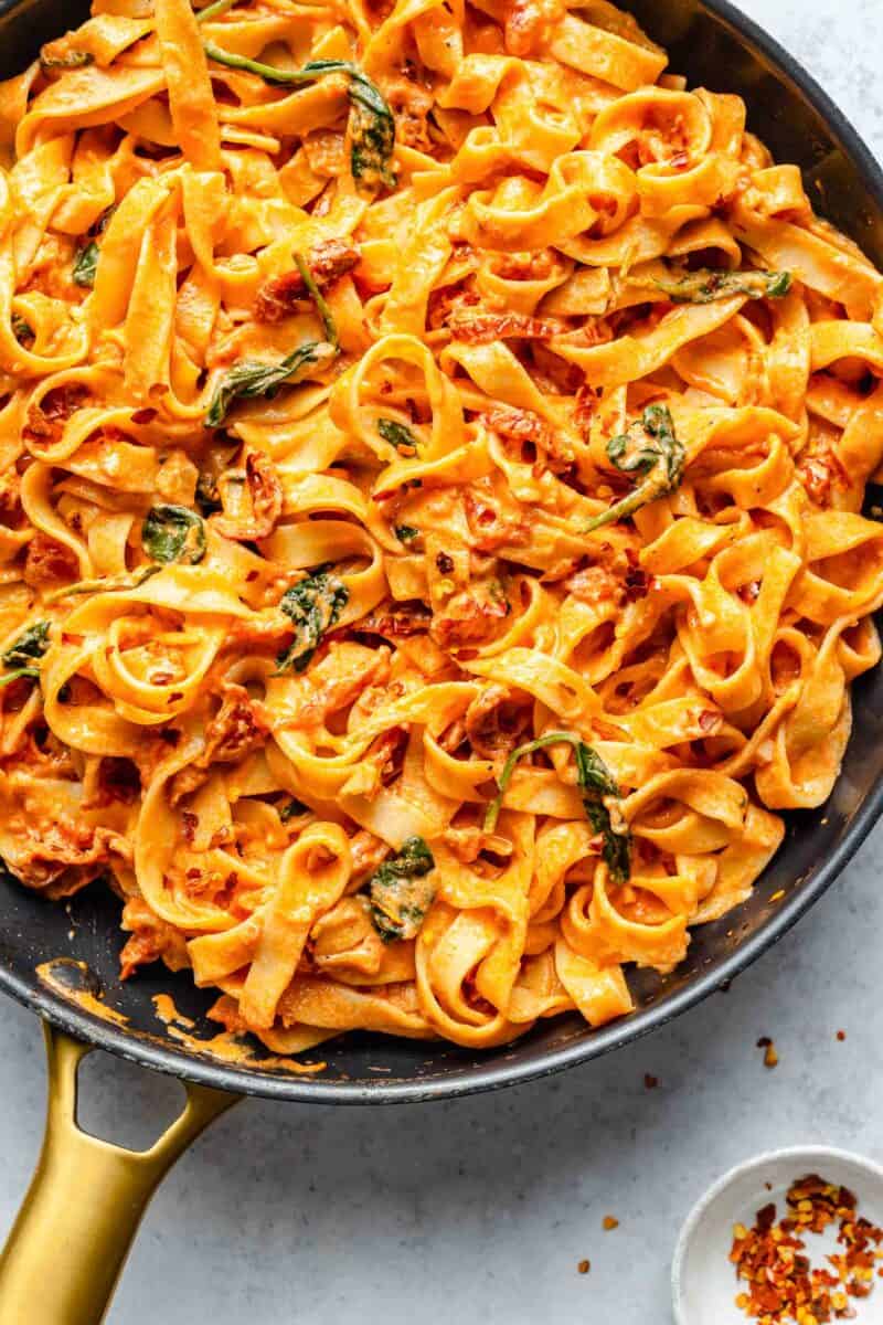 sun-dried tomato pasta in a large black skillet next to red pepper flakes